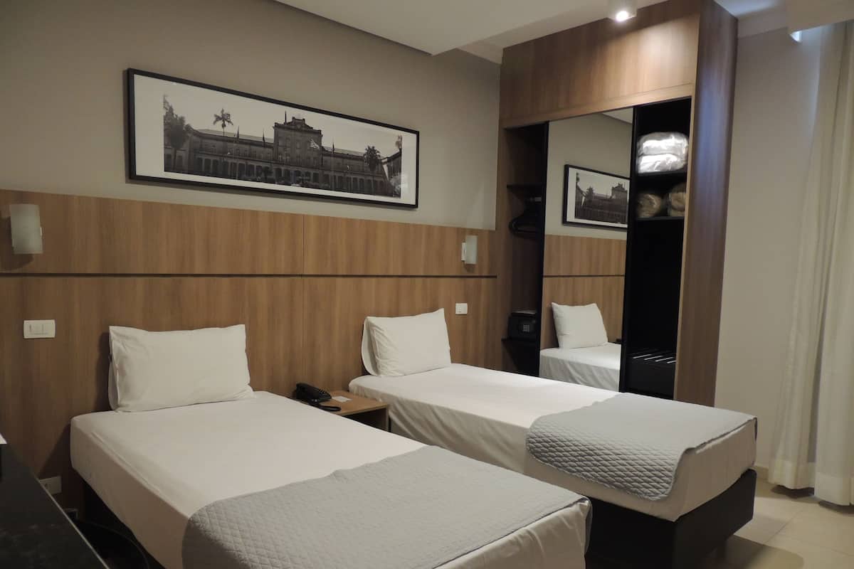 A hotel room with two single beds, a wooden headboard, a framed picture on the wall, and a mirror.