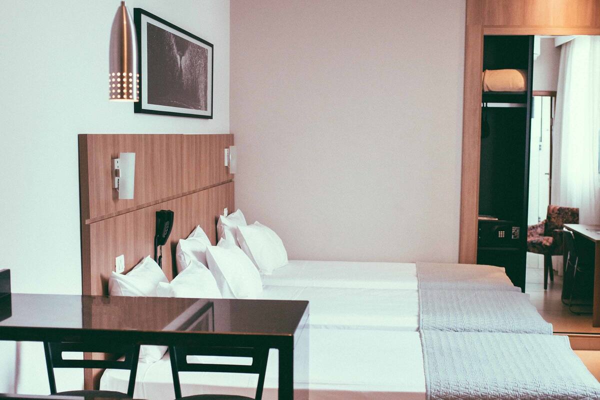 A hotel room with a bed, bedside table, chair, and a small kitchenette area.
