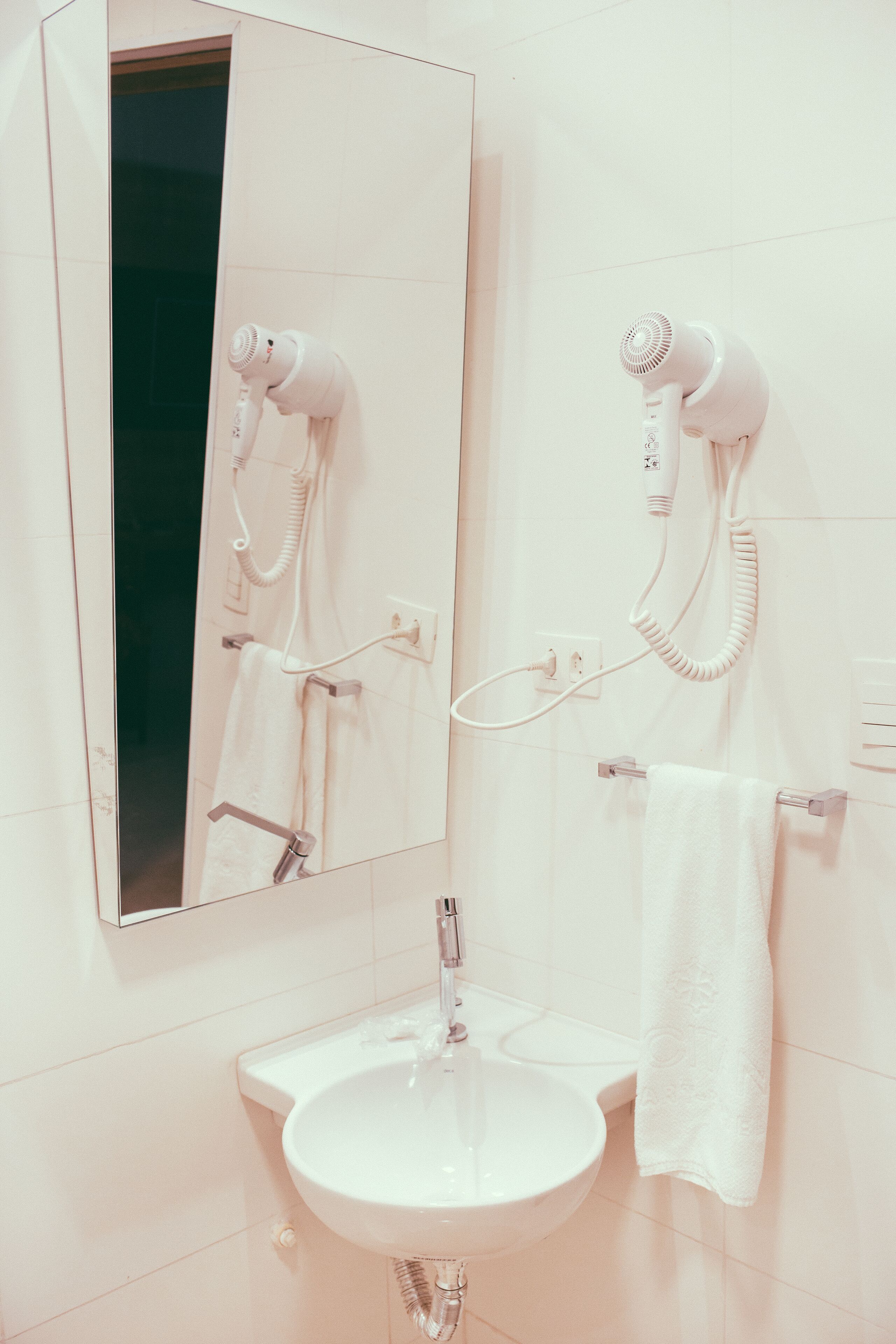 A bathroom with a white sink, a mirror, and two hair dryers mounted on the wall.