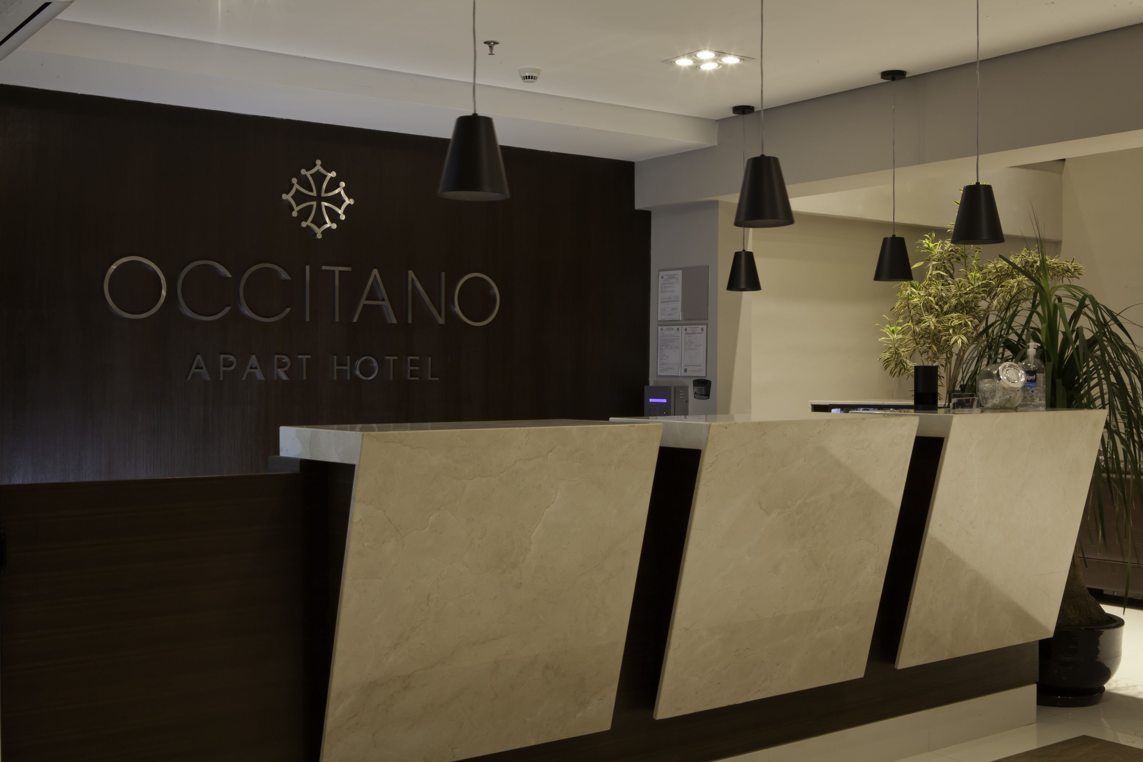 Una recepción con detalles en madera oscura y un cartel que dice "OCCITANO APART HOTEL".
