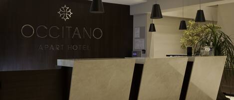 Una recepción con detalles en madera oscura y un cartel que dice "OCCITANO APART HOTEL".