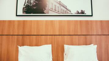 Habitación de hotel con cabecera de madera, dos almohadas blancas y un cuadro con una imagen de un edificio en la pared.