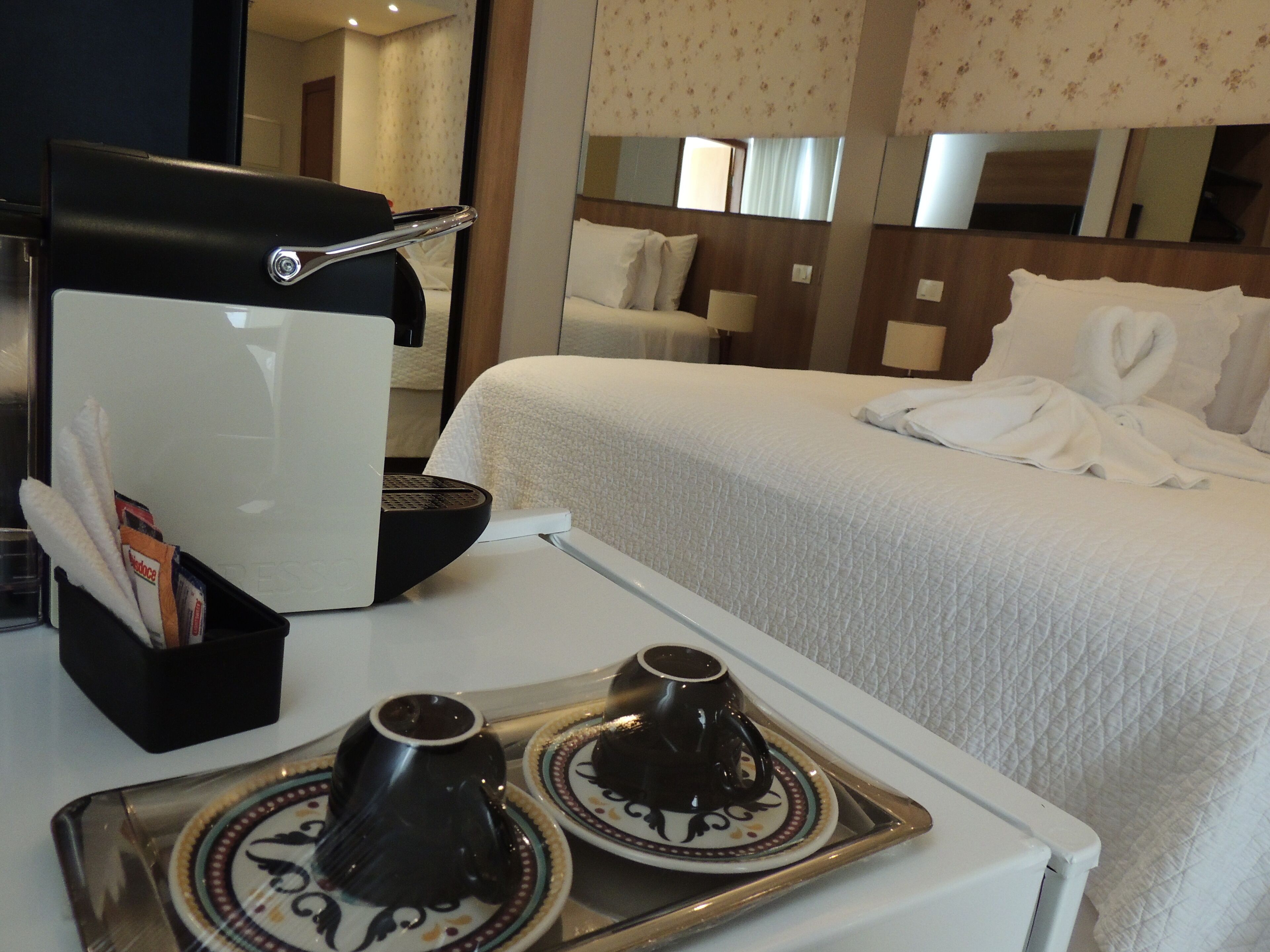 Ett hotellrum med en säng, en kaffemaskin och ett bricka med två koppar.