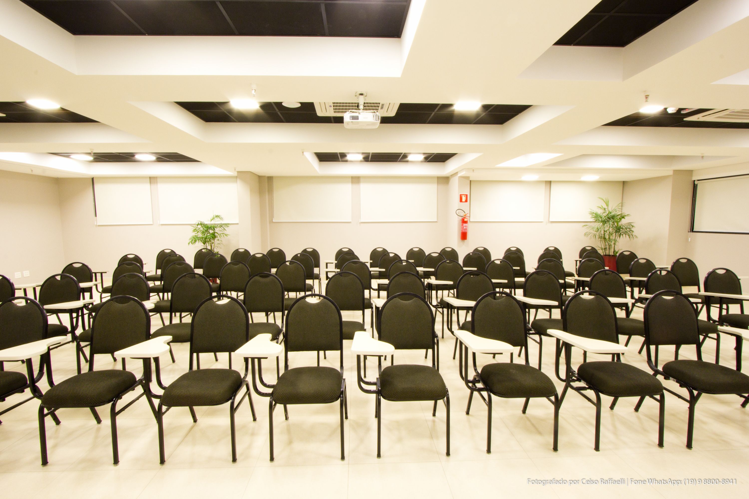 Une salle de conférence avec des rangées de chaises et de tables, un projecteur et un tableau blanc.