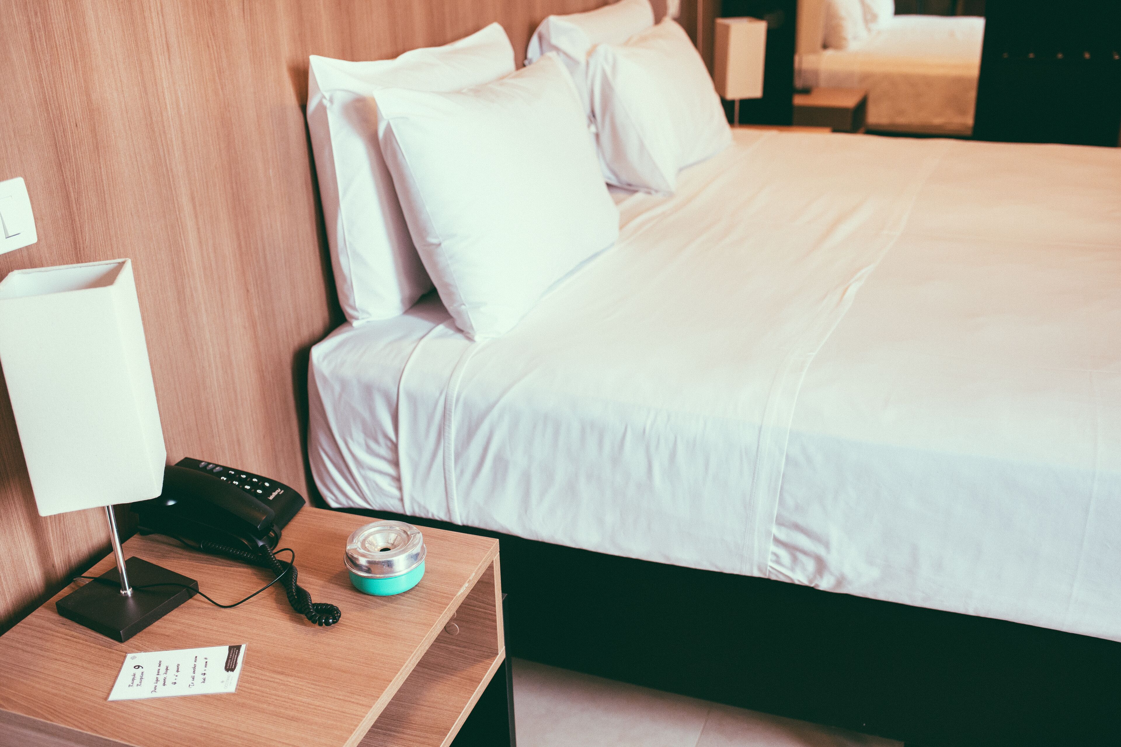 Habitación de hotel con una cama bien hecha, una mesita de noche con lámpara, teléfono y un pequeño recipiente.