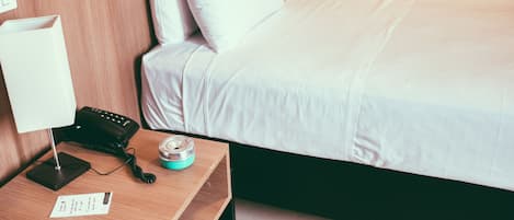 Habitación de hotel con una cama bien hecha, una mesita de noche con lámpara, teléfono y un pequeño recipiente.