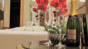 Una mesa con una botella de champagne Chandon, dos copas y un jarrón con orquídeas rojas.