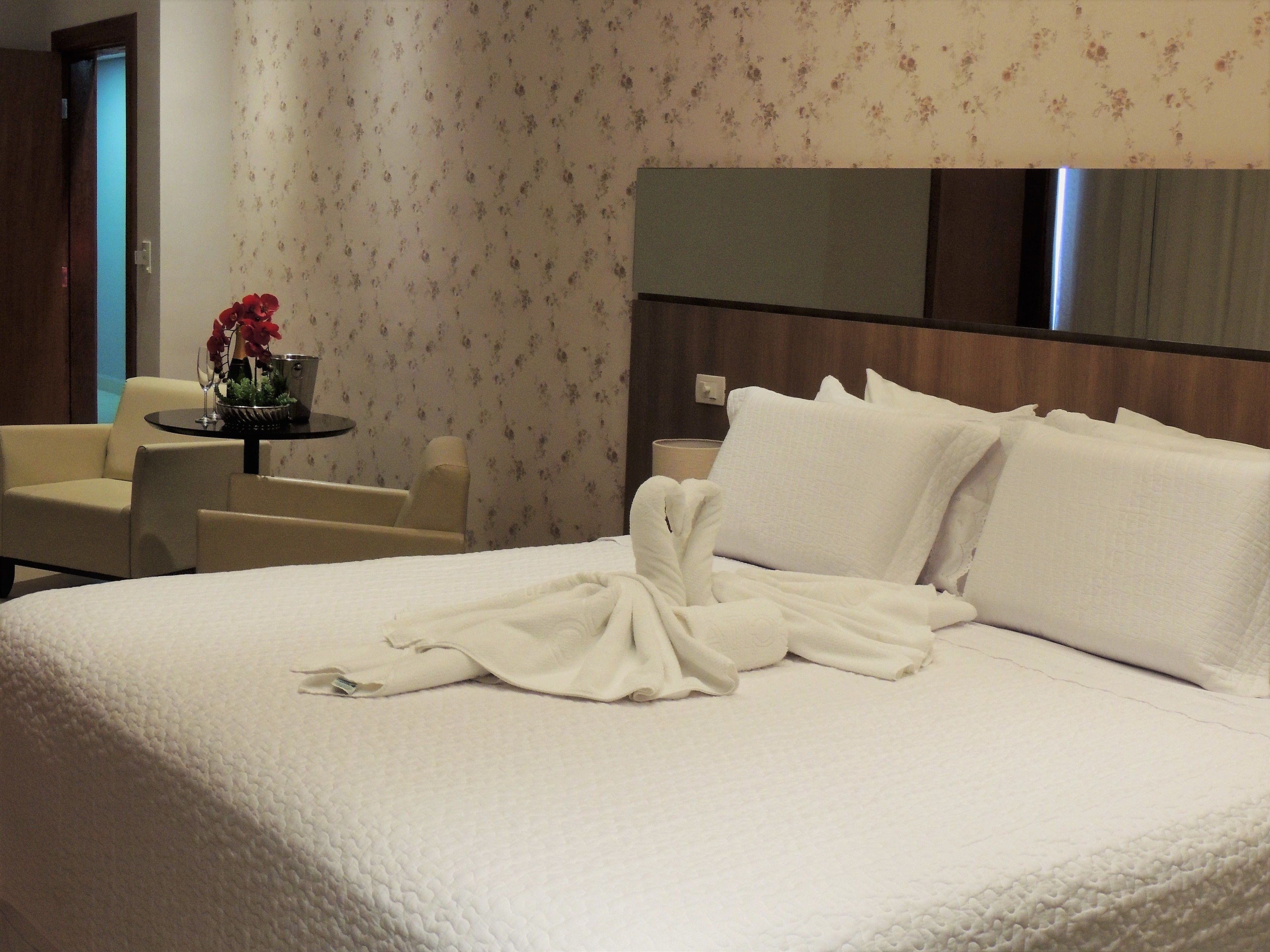 A hotel room with a large bed, a sitting area with a table and chairs, and a floral wallpaper design.