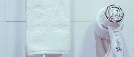 A white towel hanging on a metal towel rack, a white hairdryer with a cord, and a white wall with a subtle embossed design.