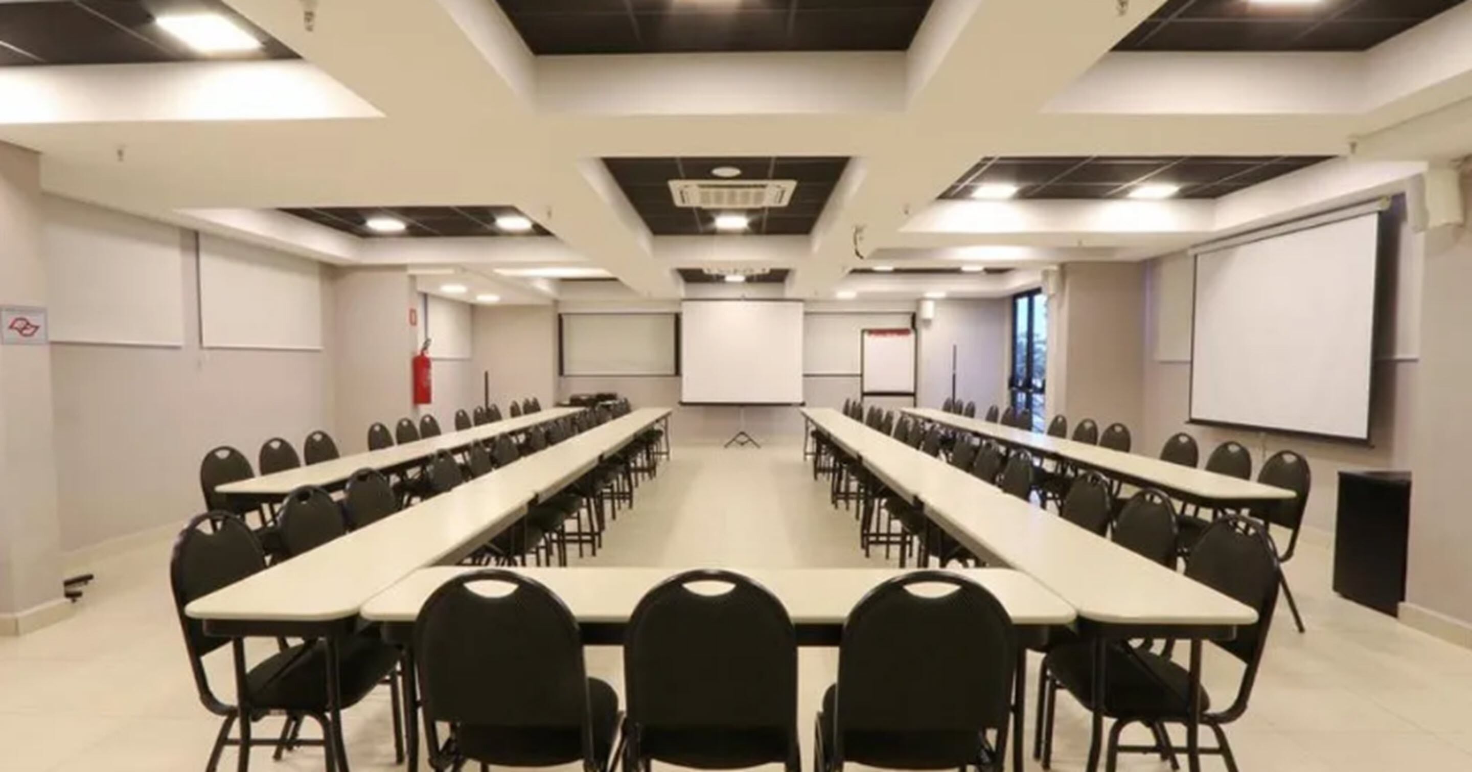 Un salón de conferencias con mesas largas y sillas, una pantalla de proyector y una pizarra.