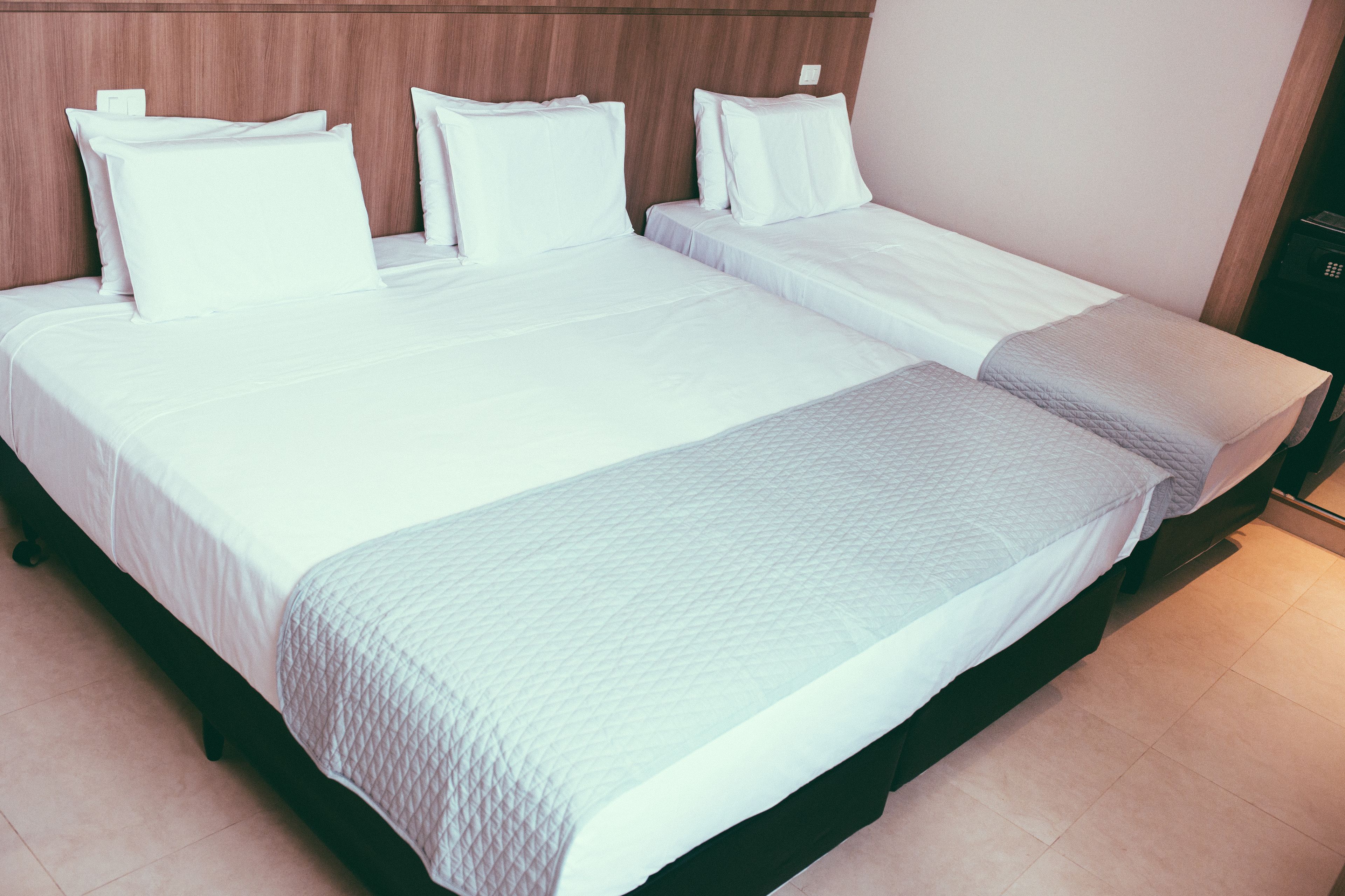 Un lit double avec du linge de lit blanc et une couverture matelassée, une tête de lit en bois et une table de chevet avec une lampe.