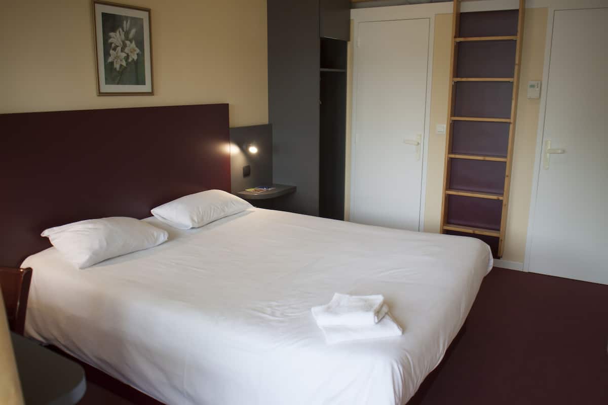 A neatly made bed with white linens and pillows, a bedside table with a lamp, and a wardrobe with a mirror.