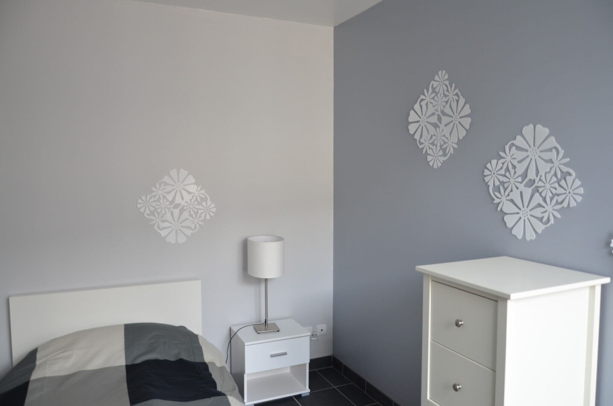 A bedroom with a bed, a nightstand, a lamp, a dresser, and decorative wall art.