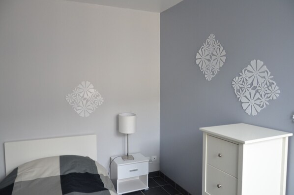 Un dormitorio con cama, mesita de noche, lámpara, cómoda y decoración de pared.