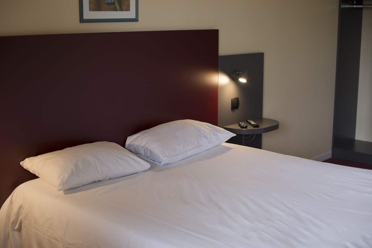 A neatly made bed with white linens and pillows, a dark headboard, and a bedside table with a lamp.