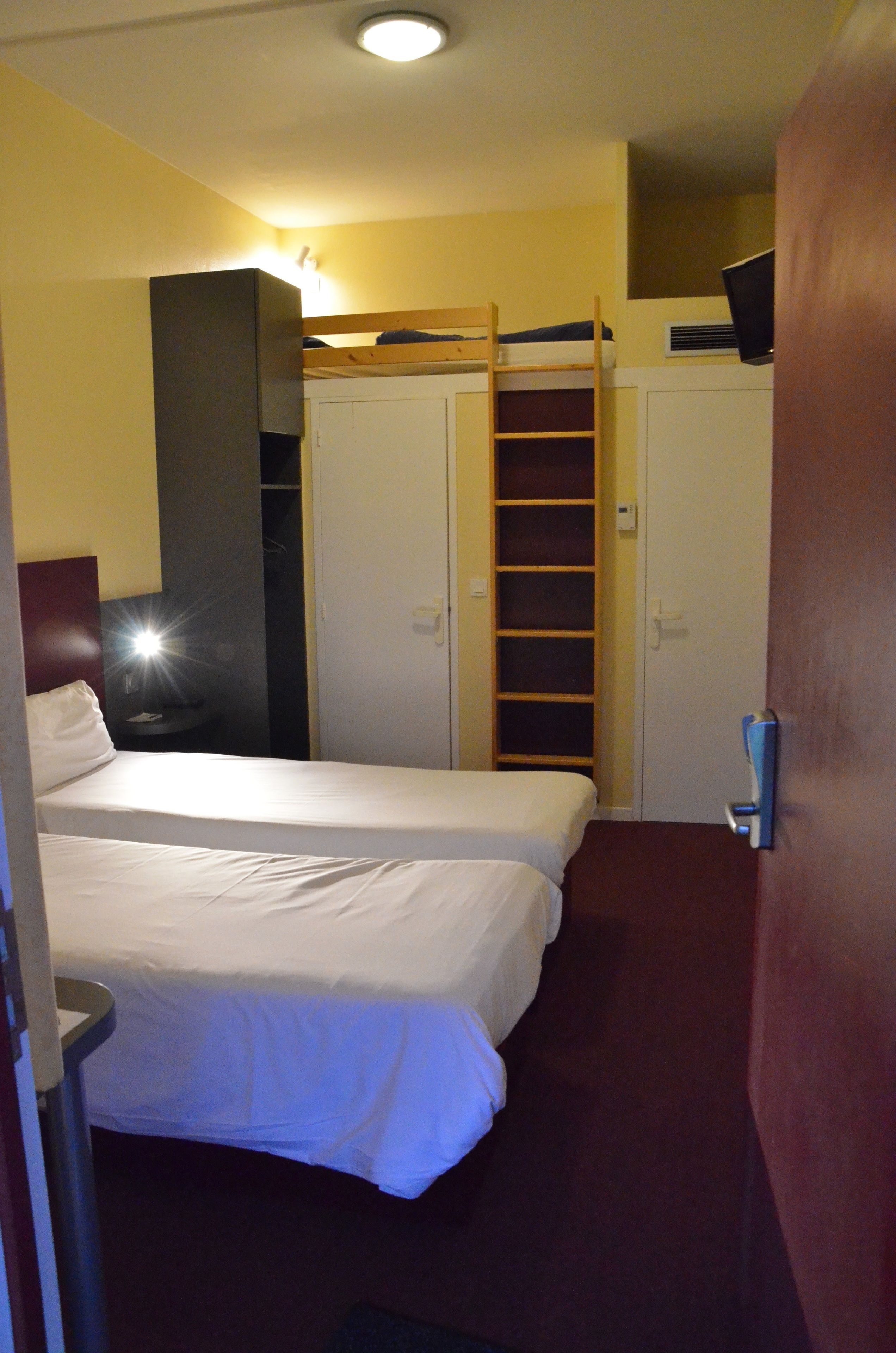 A hotel room with two beds, a wardrobe, and a built-in shelf.
