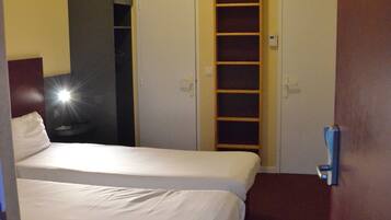 A hotel room with two beds, a wardrobe, and a built-in shelf.