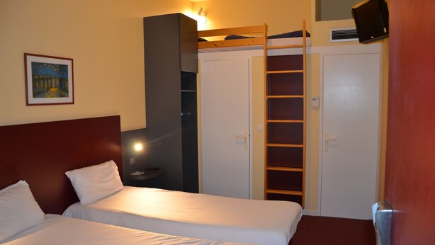 Quarto de hotel com duas camas, um guarda-roupa, uma televisão e um quadro na parede.