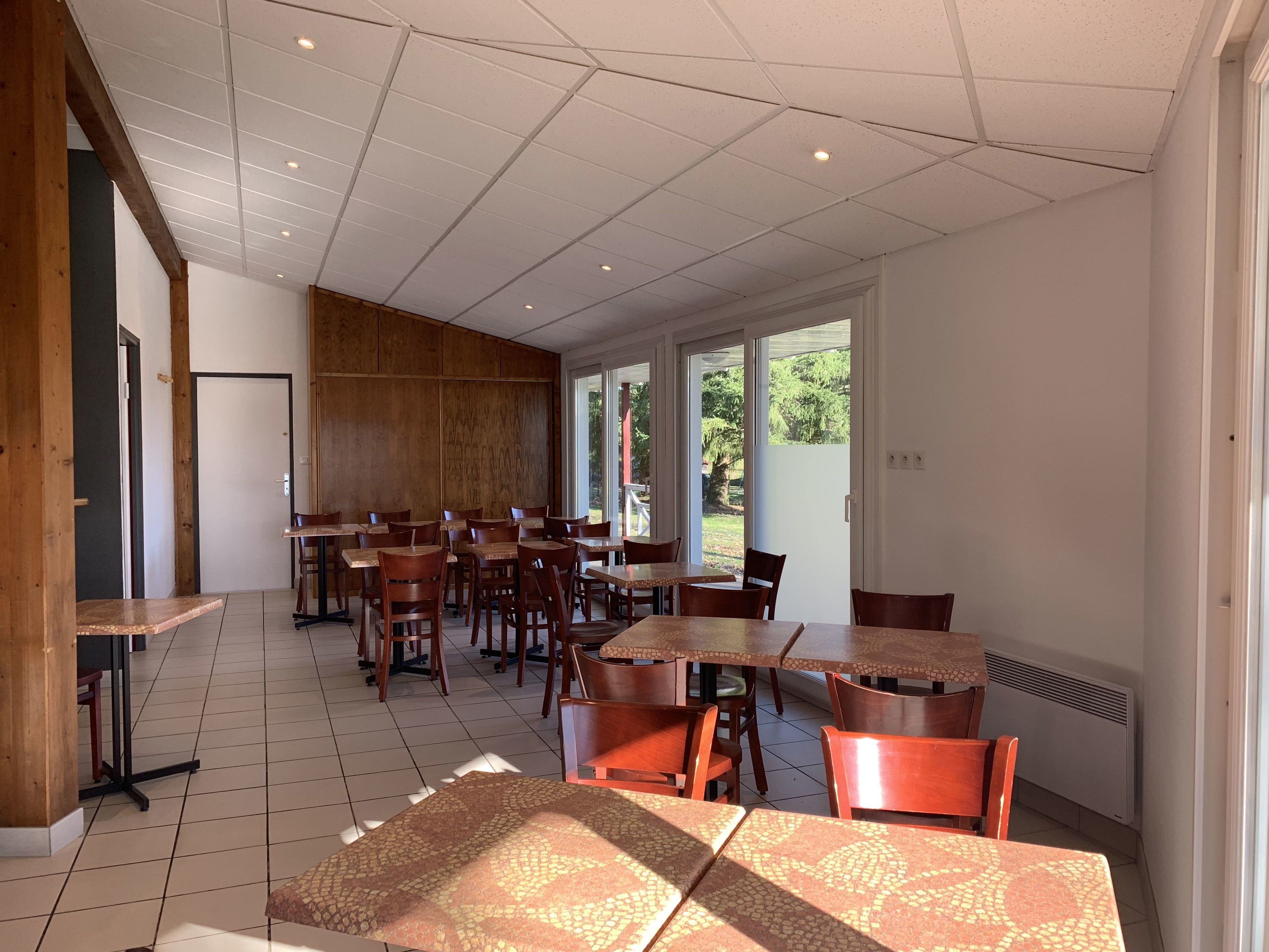 A spacious indoor dining area with multiple tables and chairs, large windows allowing natural light, and a view of the outdoors.