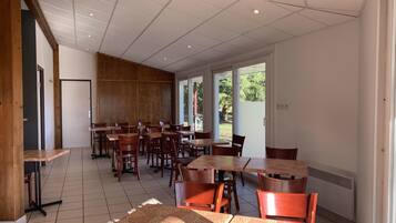A spacious indoor dining area with multiple tables and chairs, large windows allowing natural light, and a view of the outdoors.