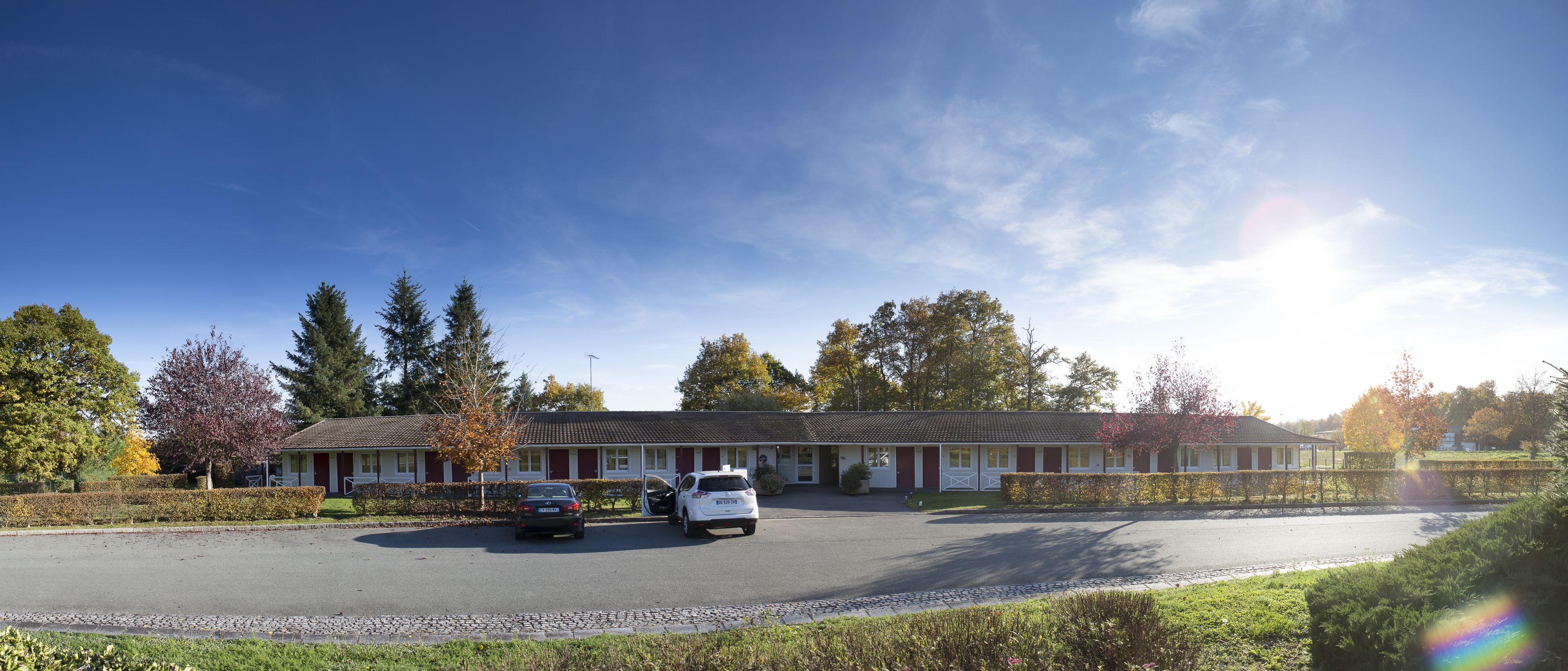 Un motel avec un parking, deux voitures garées et un ciel dégagé.