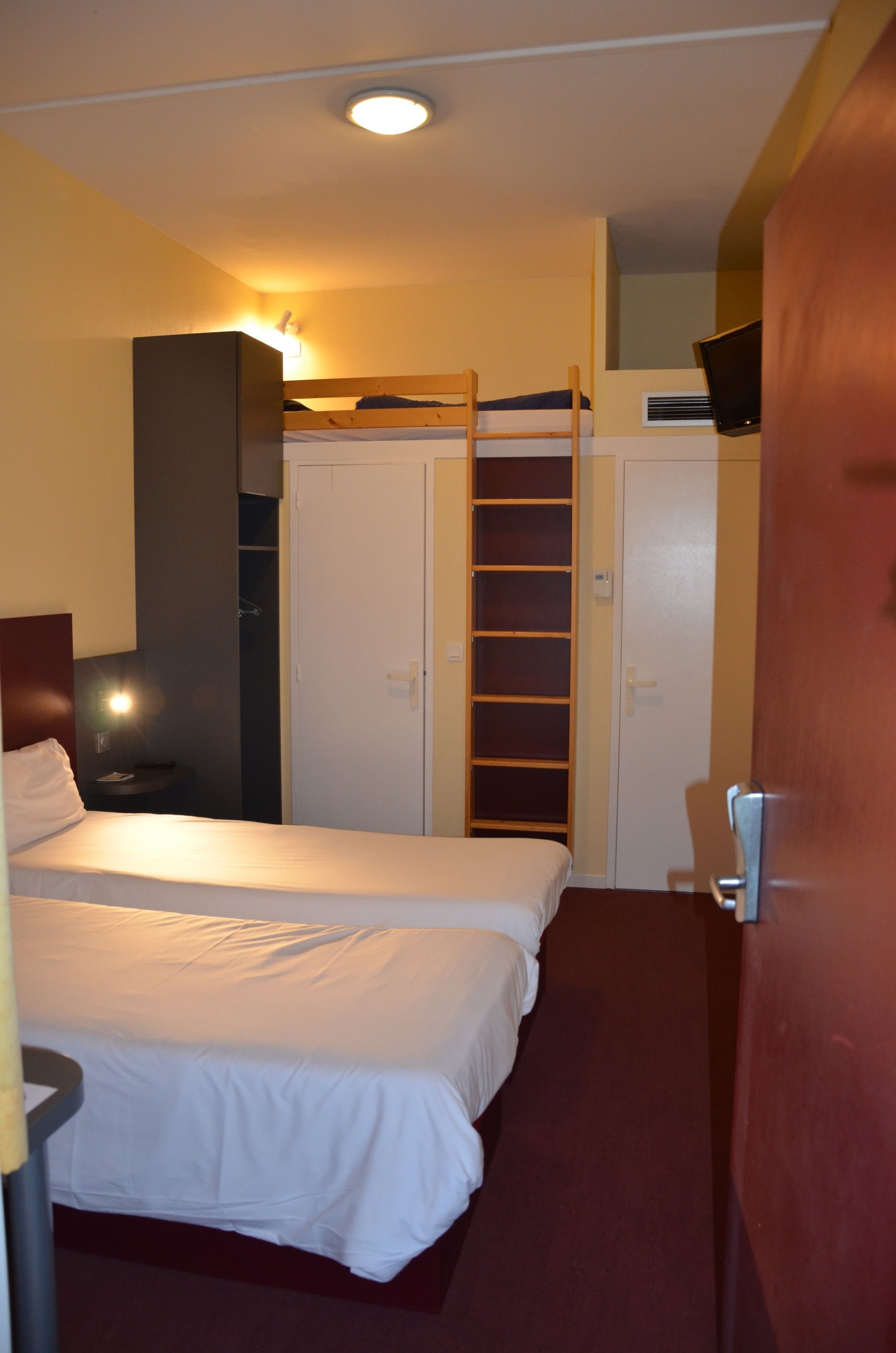 A hotel room with a bed, a wardrobe, a desk, and a TV.