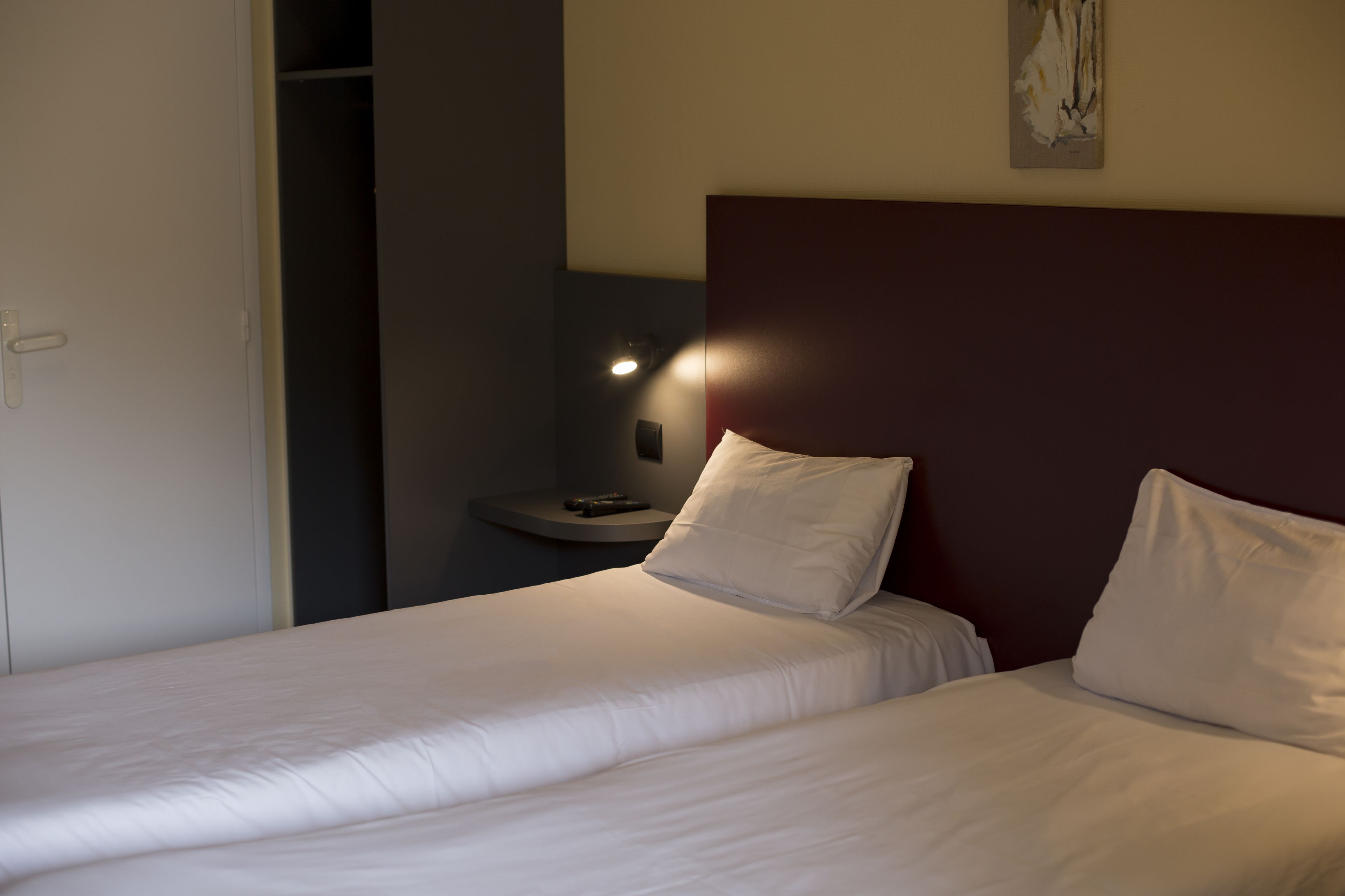 Een hotelkamer met twee bedden, een nachtkastje, een wandlamp en een deur naar een inloopkast.