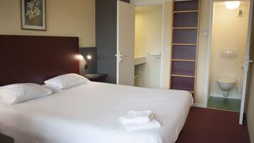 A neatly made bed with white linens and pillows, a bedside table with a lamp, and an open closet revealing shelves and a ladder.