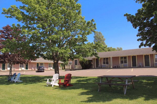 A motel with a parking lot, outdoor seating area with chairs, and a picnic table. - Silverwood Motel (Cavendish)