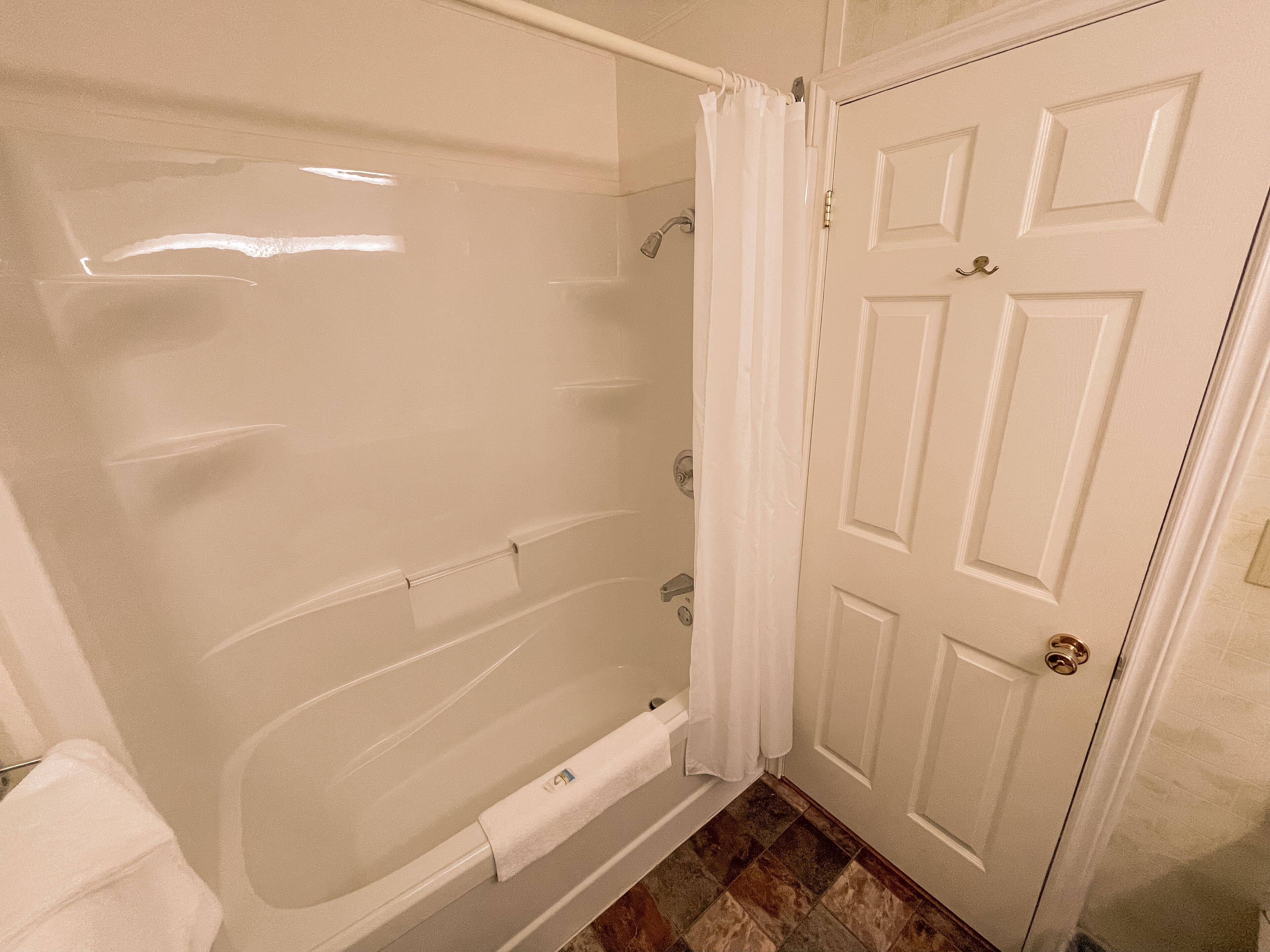 A bathroom with a bathtub, shower, and a white door.