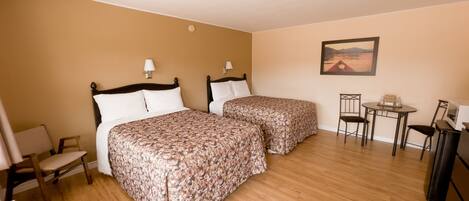 A hotel room with two beds, a small table, a chair, and a painting on the wall.