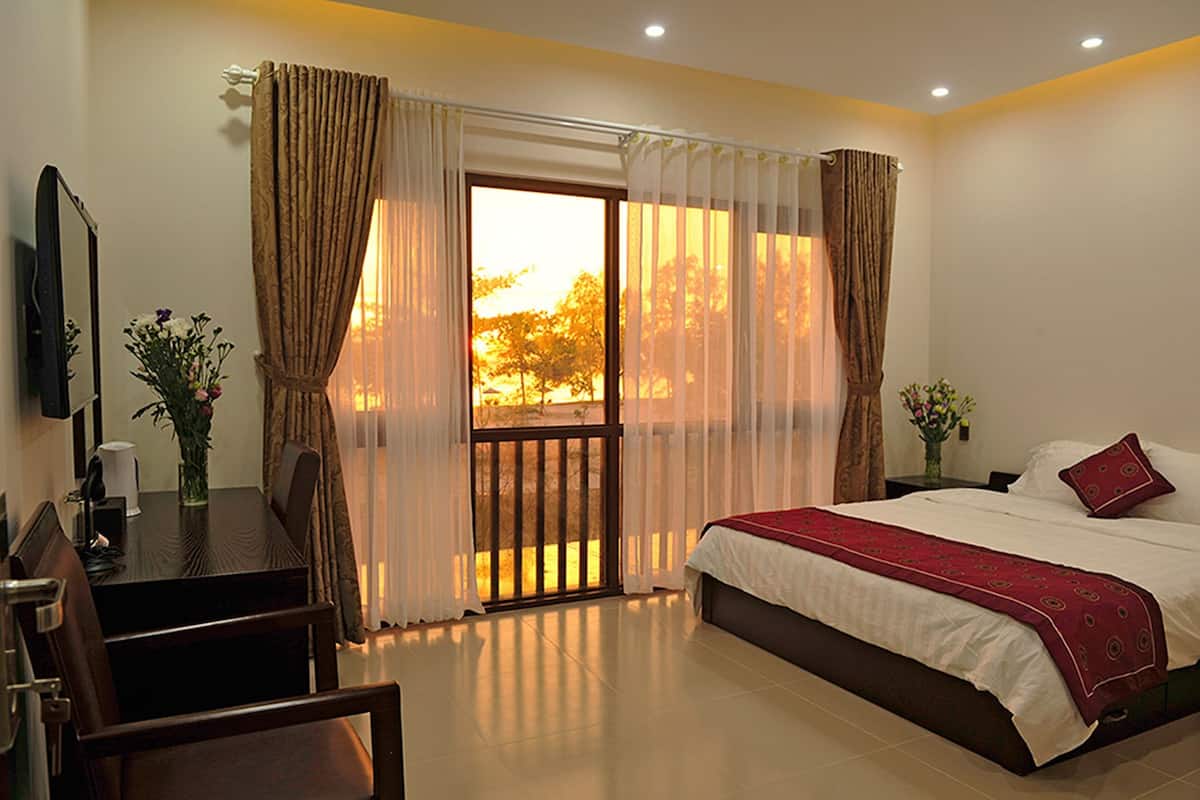 A hotel room with a bed, a desk, and a view of trees through the window.