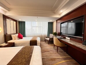 Habitación de hotel con dos camas, un escritorio, un televisor y una ventana con cortinas.