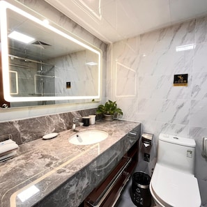 Un baño moderno con lavamanos de mármol, un espejo grande, un inodoro y un cesto de basura.