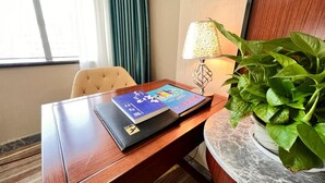 Habitación de hotel con escritorio de madera, una computadora portátil, lámpara, planta en maceta y ventana con cortinas.