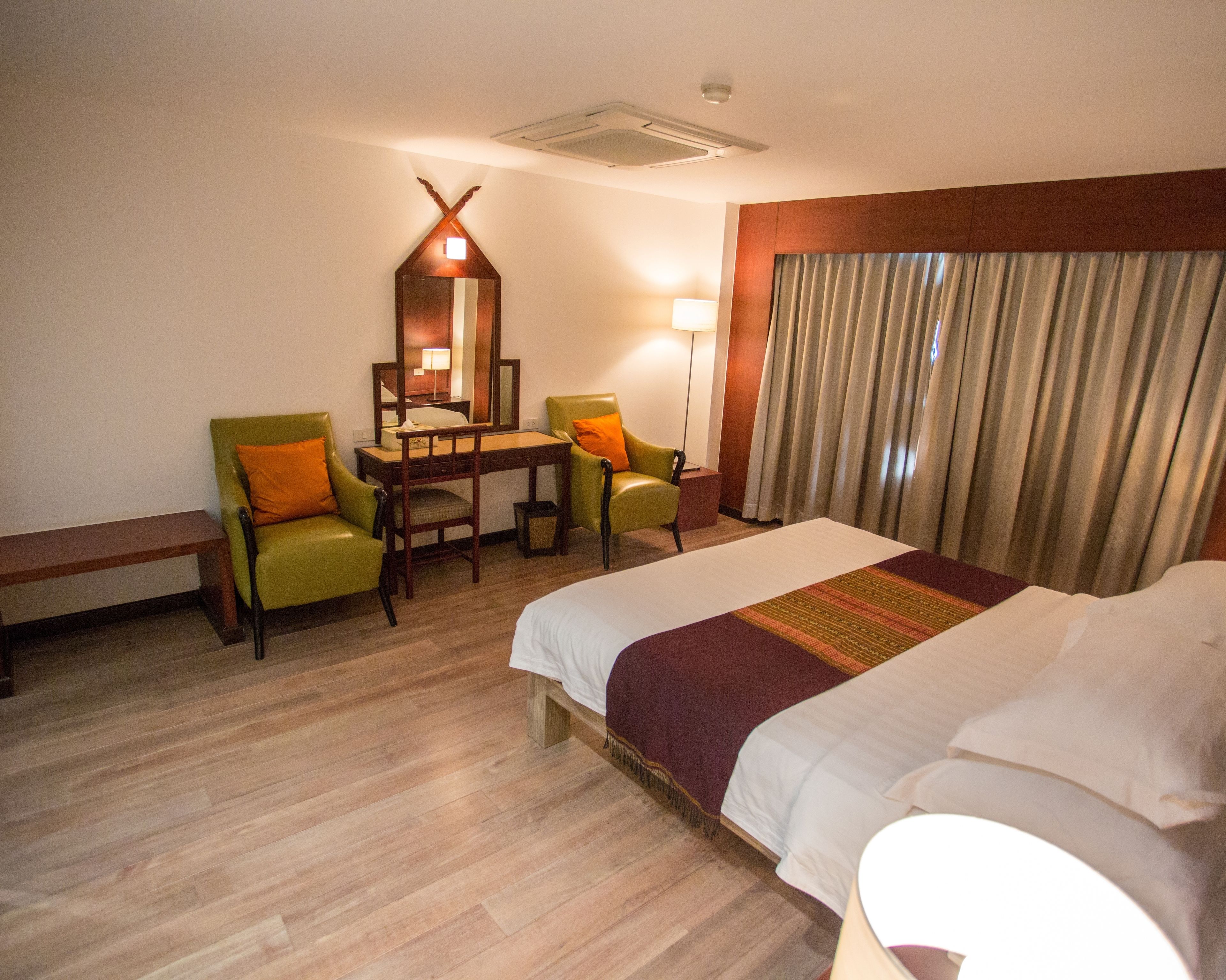 A hotel room with a bed, two chairs, a desk, a mirror, a lamp, and a window with curtains.