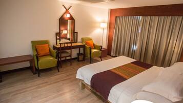 A hotel room with a bed, two chairs, a desk, a mirror, a lamp, and a window with curtains.