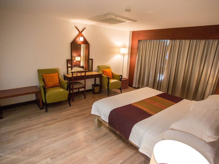 A hotel room with a bed, two chairs, a desk, a mirror, a lamp, and a window with curtains.