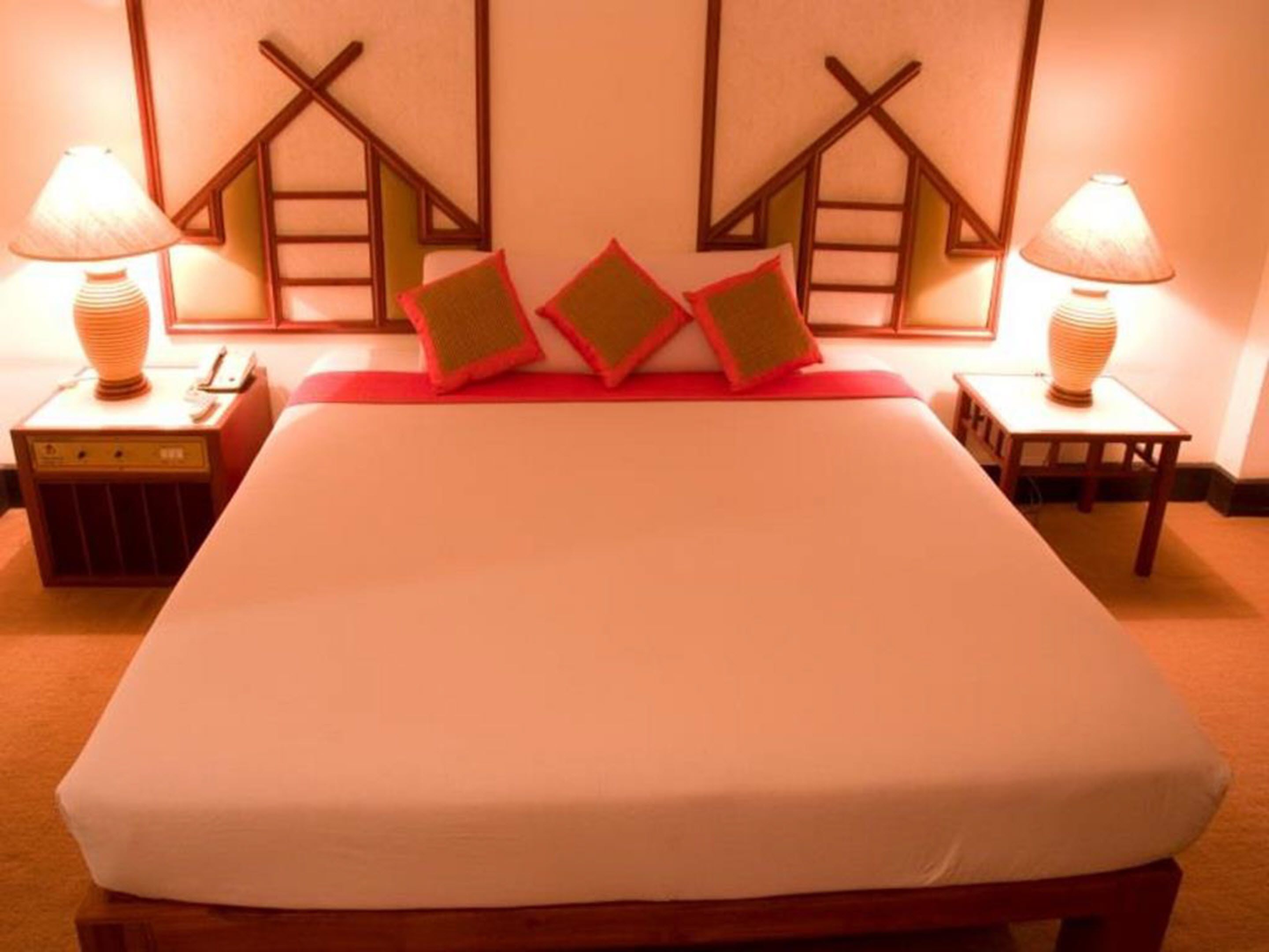 Una cama bien hecha con un cabecero rojo, dos lámparas de noche y una mesita de noche de madera.