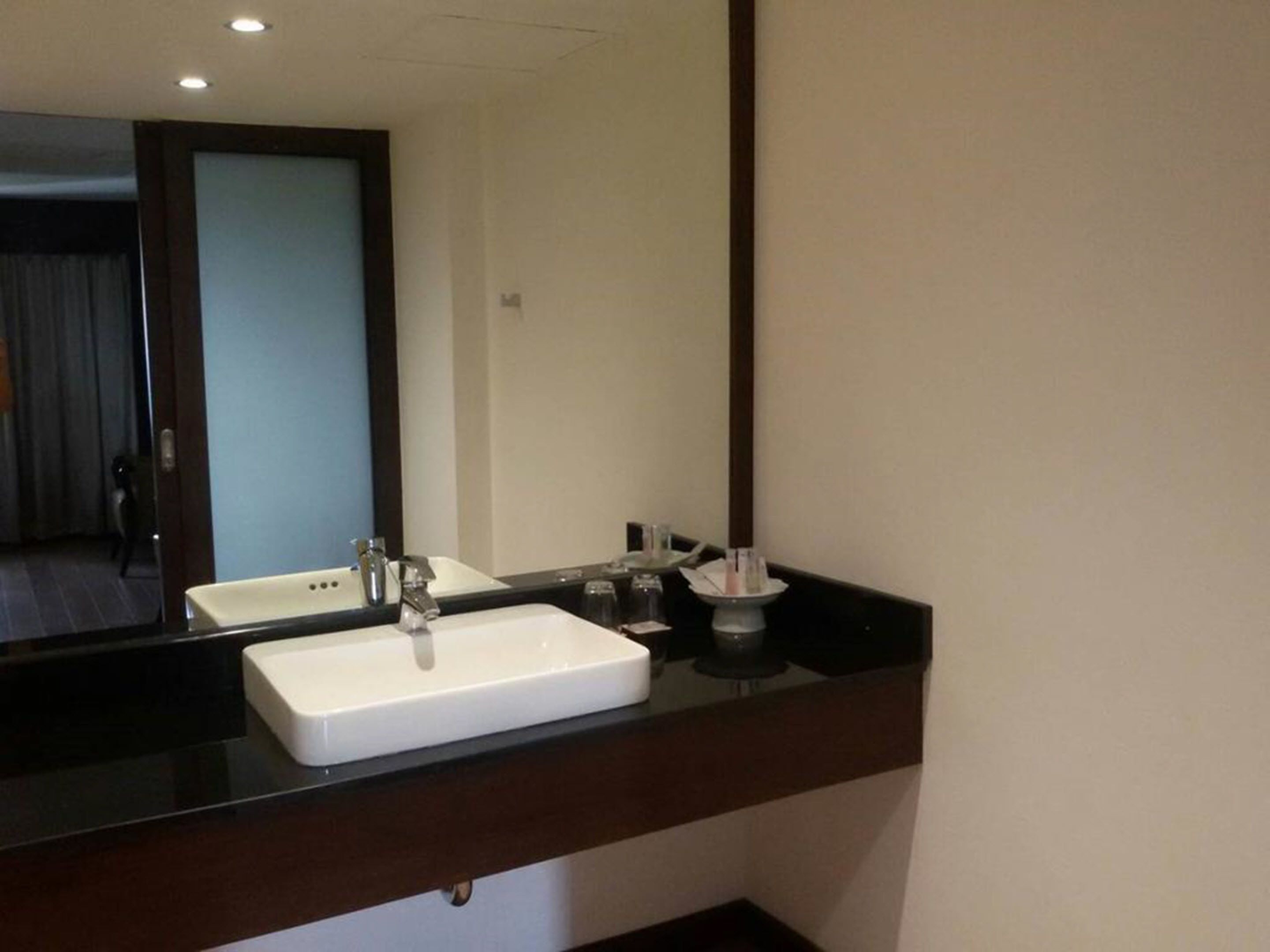 Une salle de bain avec un lavabo blanc, un miroir et un plan de toilette foncé.