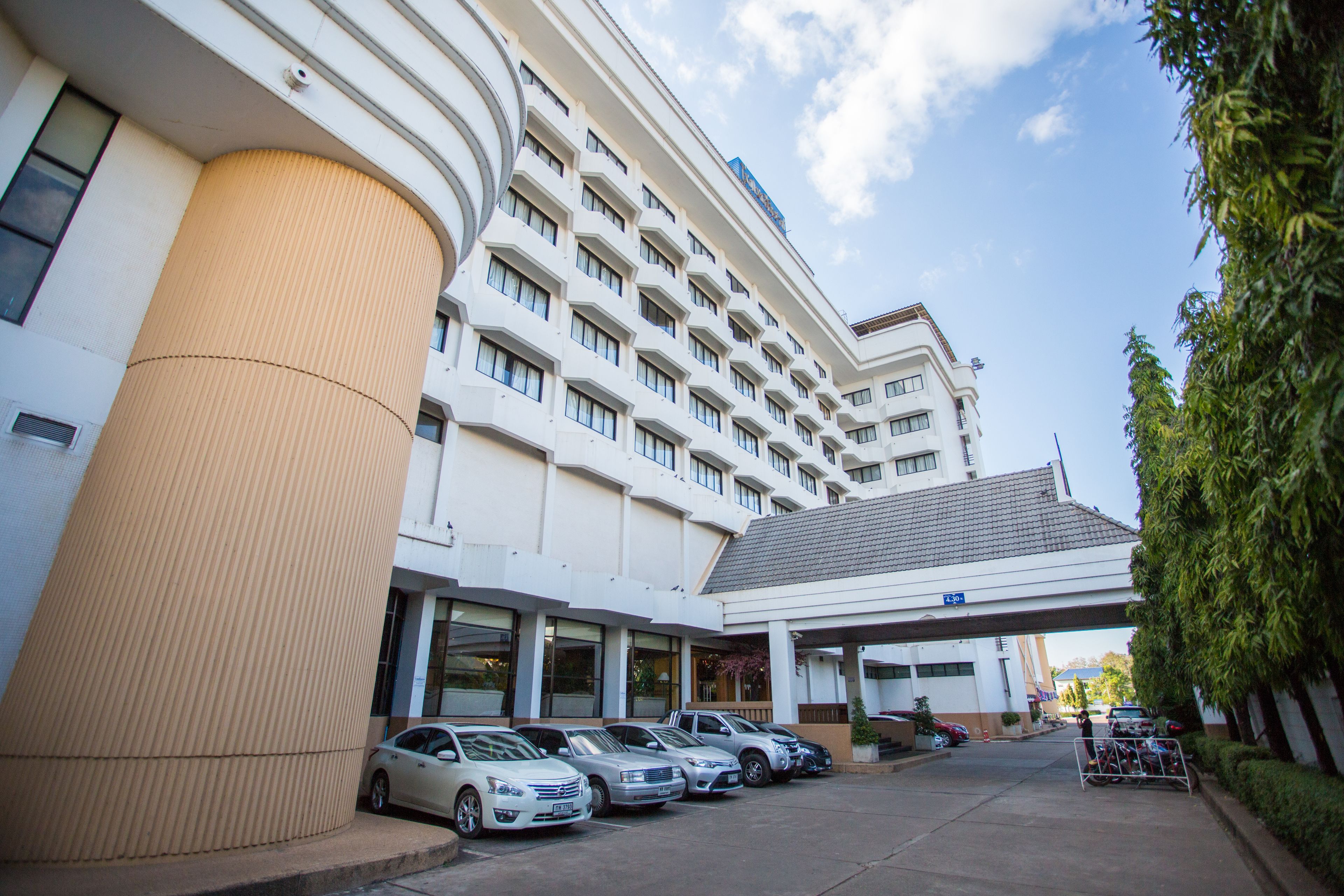 Un hotel con una columna cilíndrica grande, varios pisos y una entrada cubierta. Hay varios coches estacionados en la parte delantera.