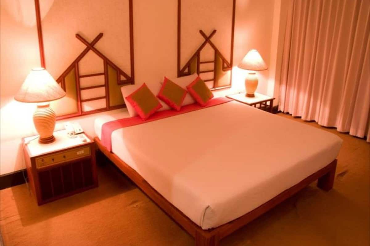 Quarto de hotel com uma cama grande, duas mesas de cabeceira, um abajur e uma cortina.