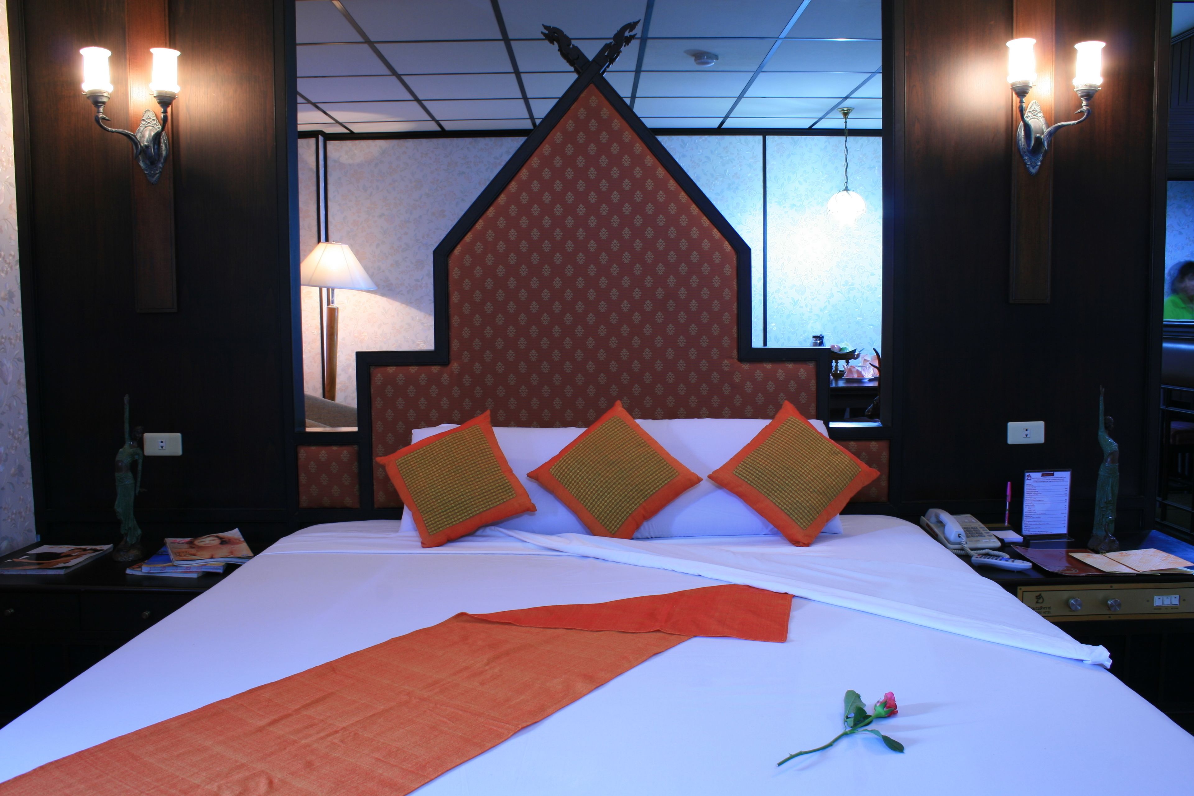 Une chambre d’hôtel avec un grand lit, une tête de lit décorative et deux lampes fixées au mur.