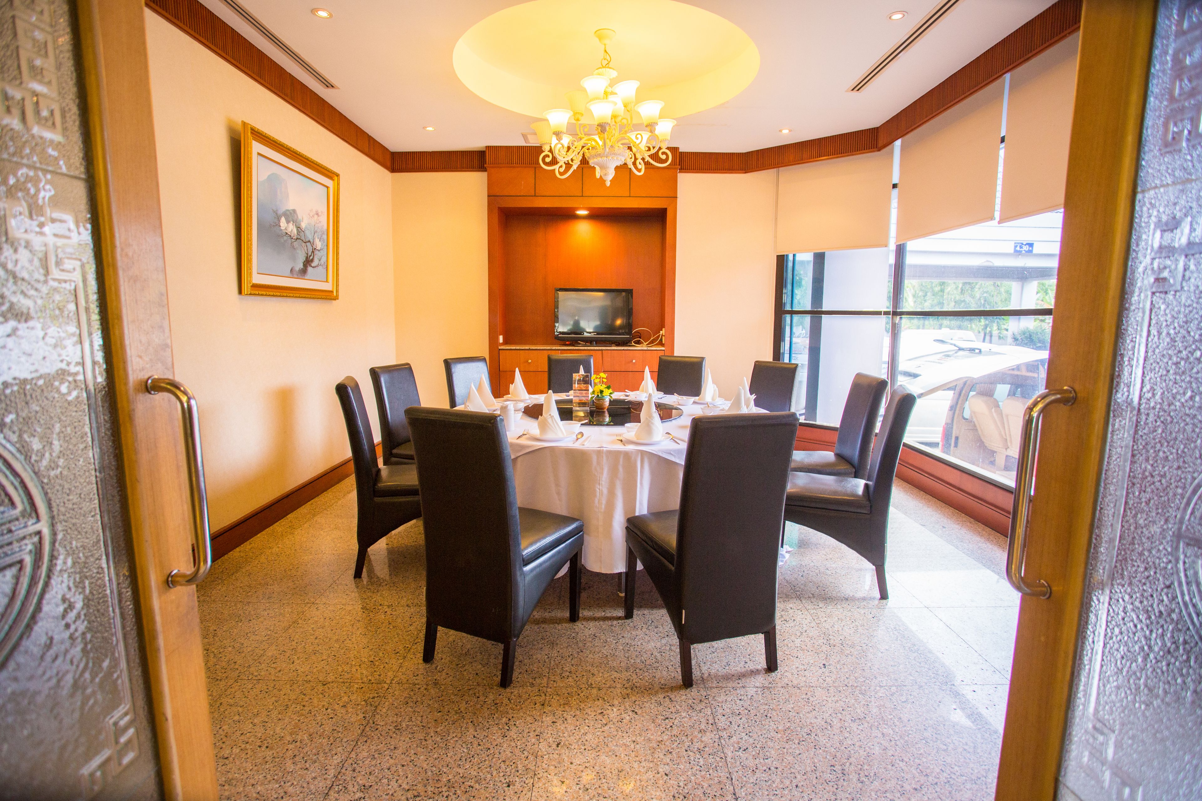 A conference room with a round table, chairs, a chandelier, a television, and a large window.