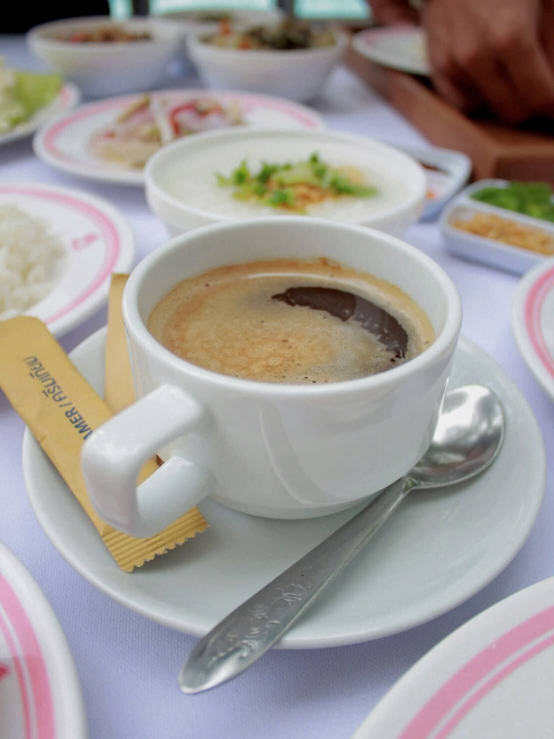 A cup of coffee with a spoon and a napkin on a table with various dishes.