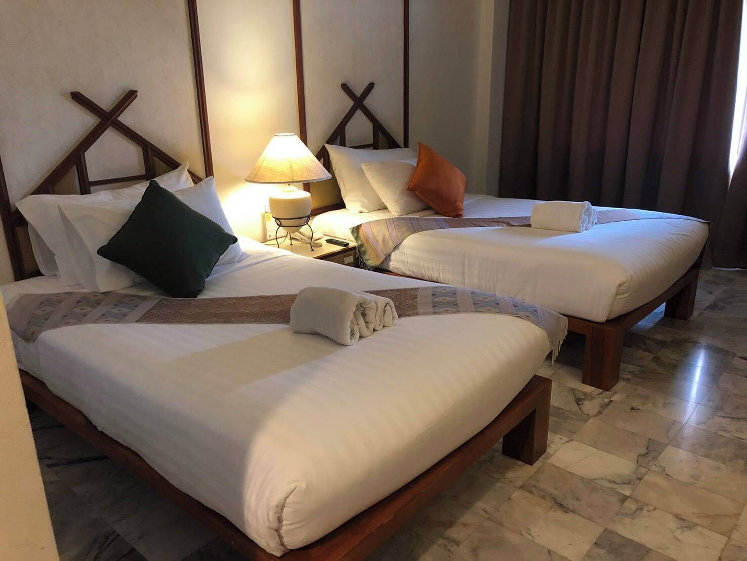 Habitación de hotel con dos camas, una mesita de noche con lámpara y un cabecero de madera.