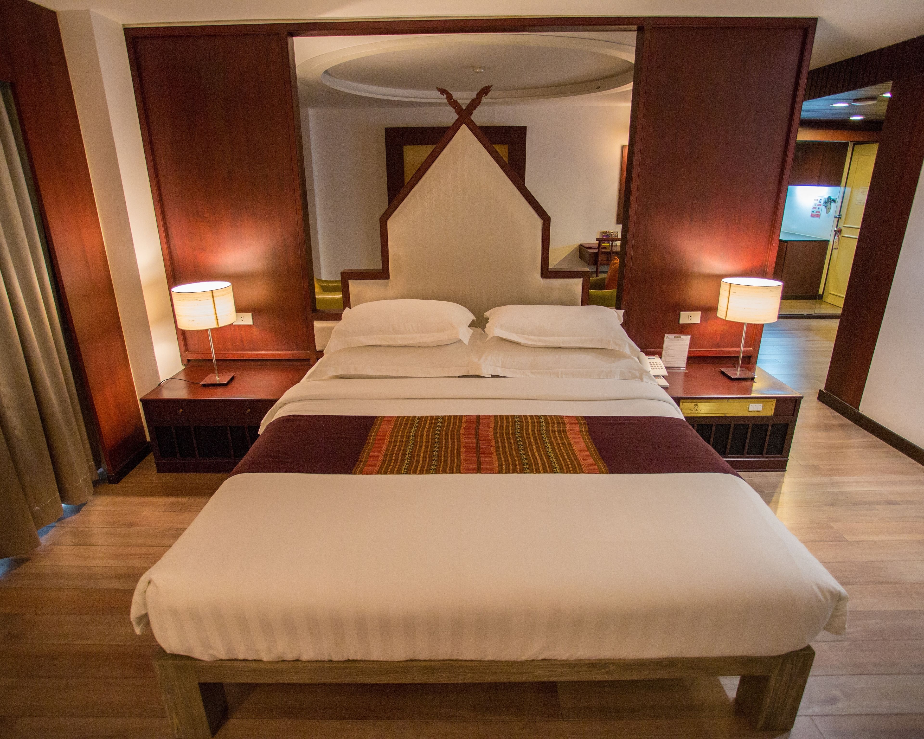 Une chambre d’hôtel avec un grand lit, deux tables de chevet, une commode, un téléviseur fixé au mur et une porte donnant sur une autre pièce.