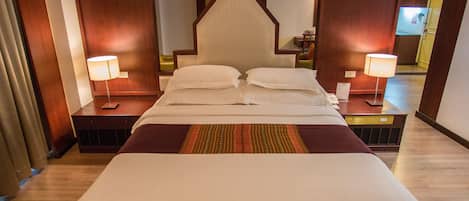 Une chambre d’hôtel avec un grand lit, deux tables de chevet, une commode, un téléviseur fixé au mur et une porte donnant sur une autre pièce.