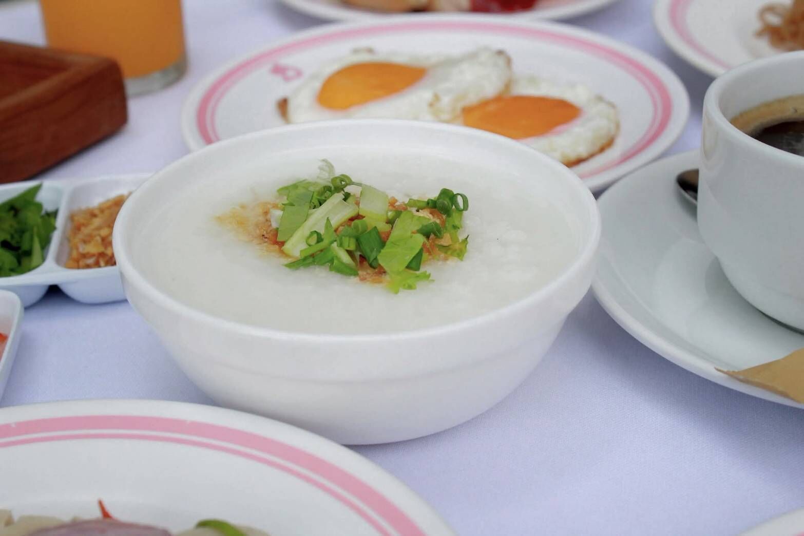 A table with various dishes including a bowl of rice topped with green onions, a plate with fried eggs, and a cup of coffee.