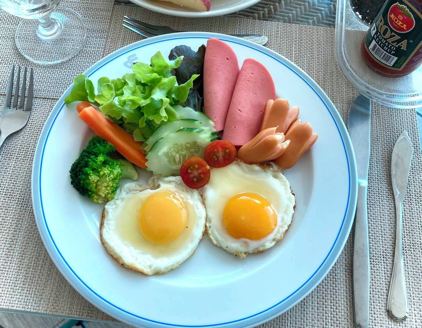 Une assiette contenant deux œufs au plat, des saucisses, de la laitue, du concombre, des brocolis et des tomates cerises.